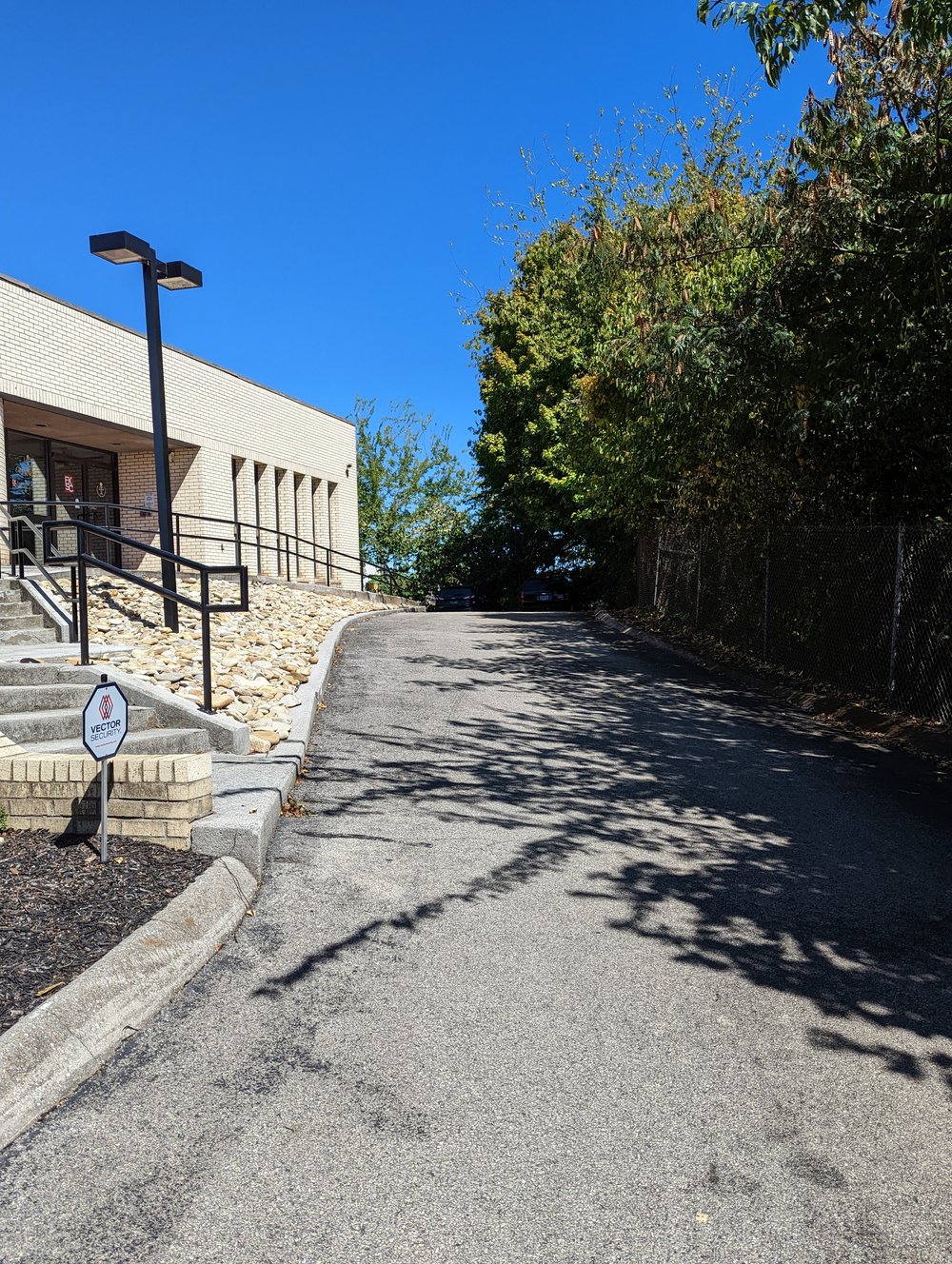 A paved driveway running along the right side of the building, sloping up toward a back lot.