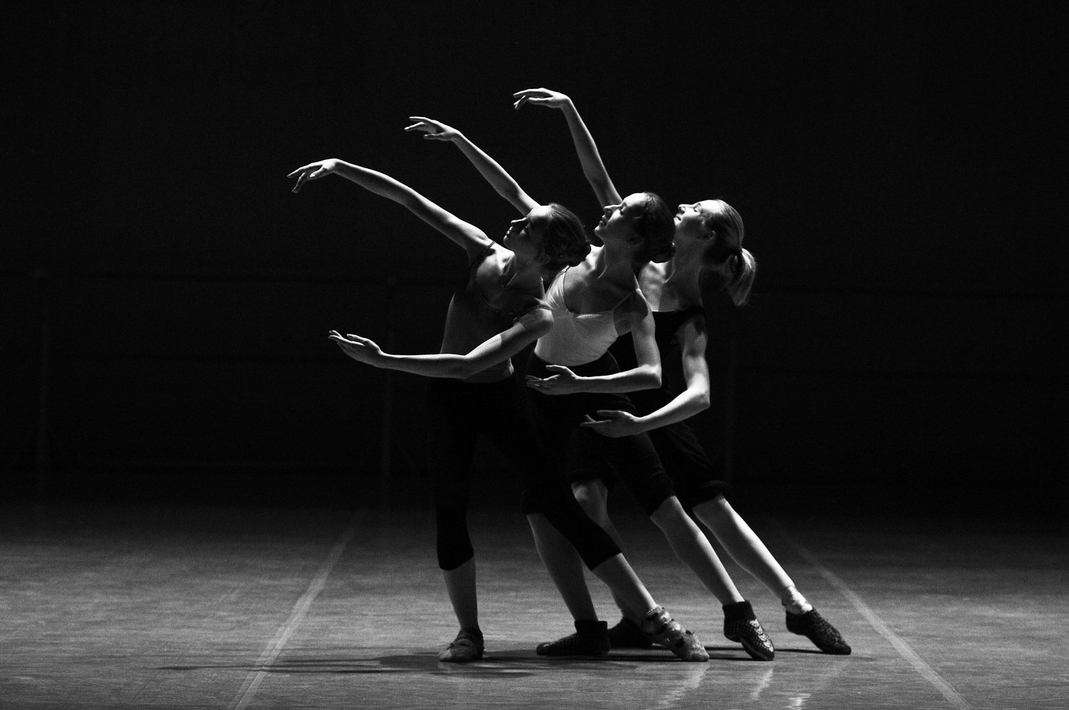 Three dancers performing together on a dark stage.